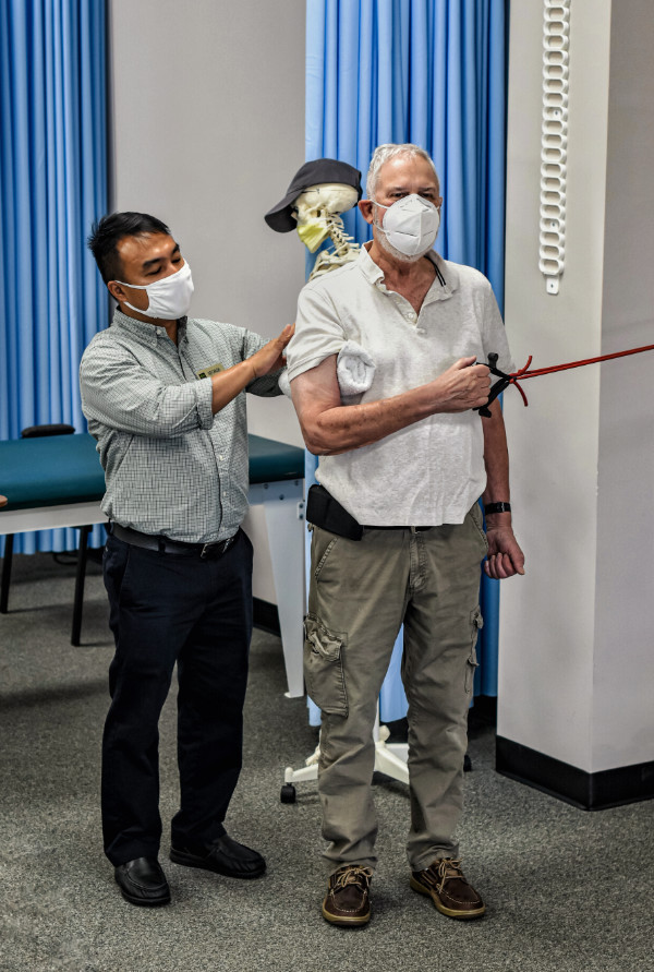 Male physical therapist oversees patient performing resistance-band shoulder exercise