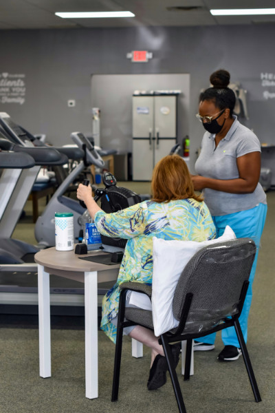 Female physical therapist looks on as female patient uses a hand exercise machine